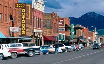 A lively small-town street with shops, cars, and mountains in the background